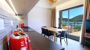 Cocina moderna con un tostador rojo, comedor con mesa y sillas, y balcón con vista al mar.