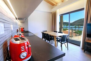 Et moderne køkken med en rød toaster, et spiseområde med bord og stole, og en balkon med havudsigt.
