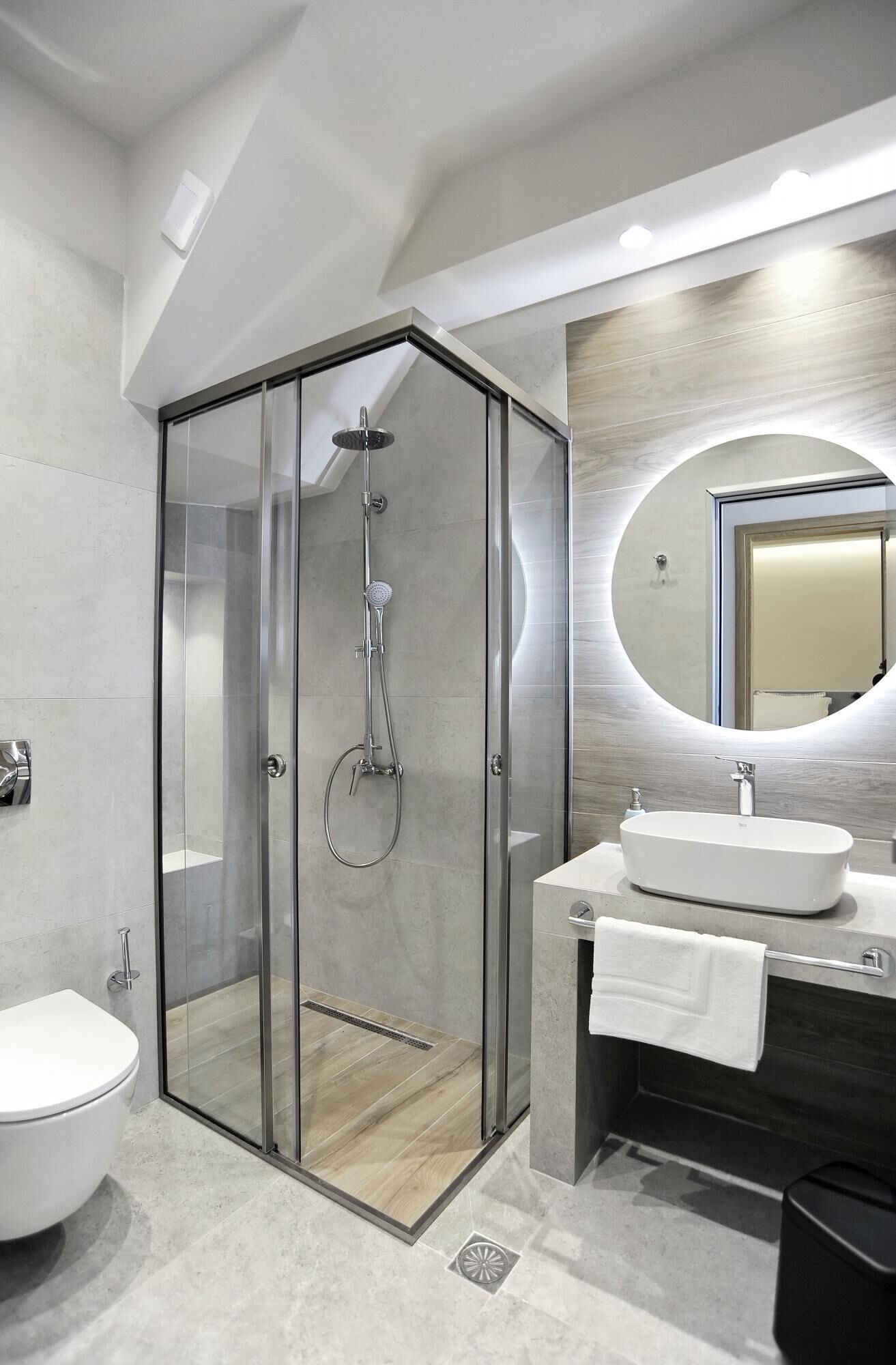 A modern bathroom with a glass-enclosed shower, a white toilet, a sink with a mirror, and a towel rack.