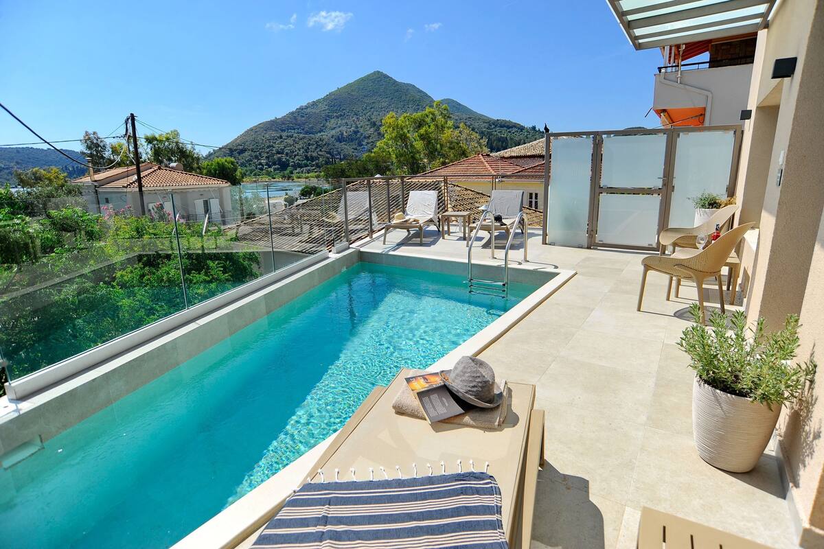 A rooftop pool with clear blue water, surrounded by lounge chairs and a potted plant.