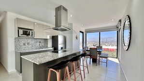 A modern kitchen with a large island, bar stools, a microwave, and a view of the city. - Altomare hermoso depa con vista al mar (Mazatlán)