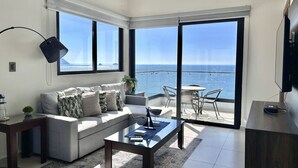 A modern living room with a sofa, coffee table, and a view of the ocean through large sliding glass doors. - Altomare hermoso depa con vista al mar (Mazatlán)
