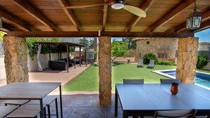 A covered patio with stone pillars, outdoor furniture, and a view of a backyard with a pool and lawn. - Incredible & Unique Costa Dorada Abode! (Creixell)