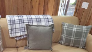 A beige leather sofa with three pillows, one grey and two with a plaid pattern. - Romantic Small Cabin in the Woods. Fireplace,Hot tub,A/C,Firepit,WiFi, Mt Rainer (Ashford)