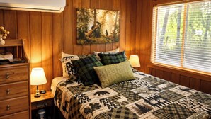 A wooden-paneled room with a bed, two bedside lamps, a painting, and a window with blinds. - Romantic Small Cabin in the Woods. Fireplace,Hot tub,A/C,Firepit,WiFi, Mt Rainer (Ashford)