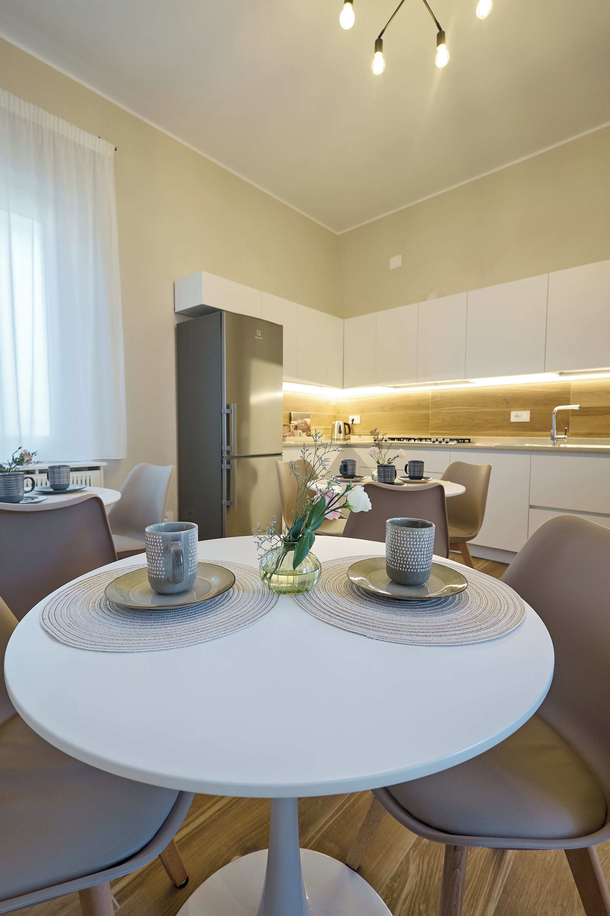 Una cocina moderna con refrigerador integrado, una mesa de comedor con dos sillas y un florero con flores sobre la mesa.