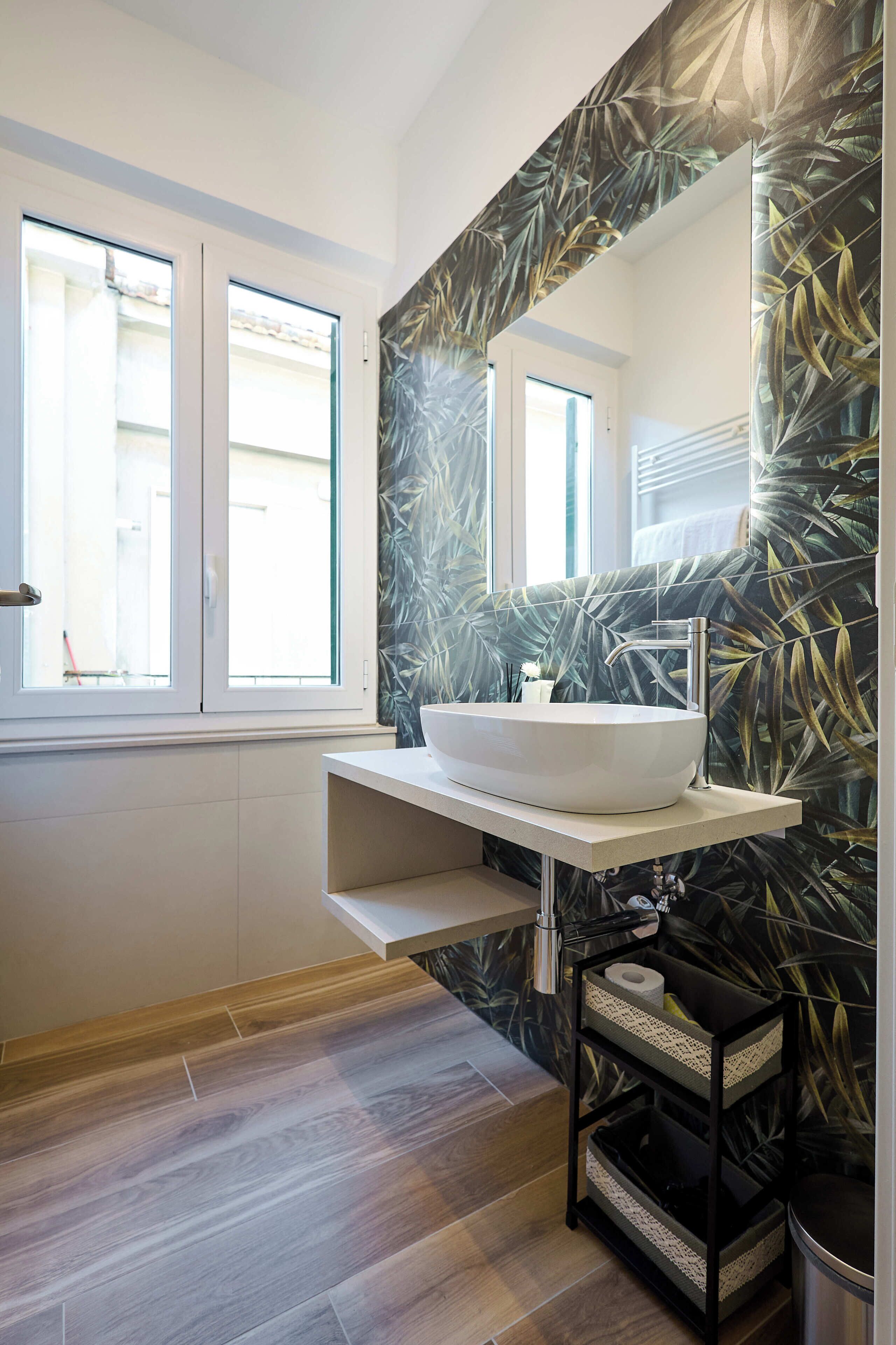 A modern bathroom with a large window, a white vessel sink, and a black vanity with storage baskets.