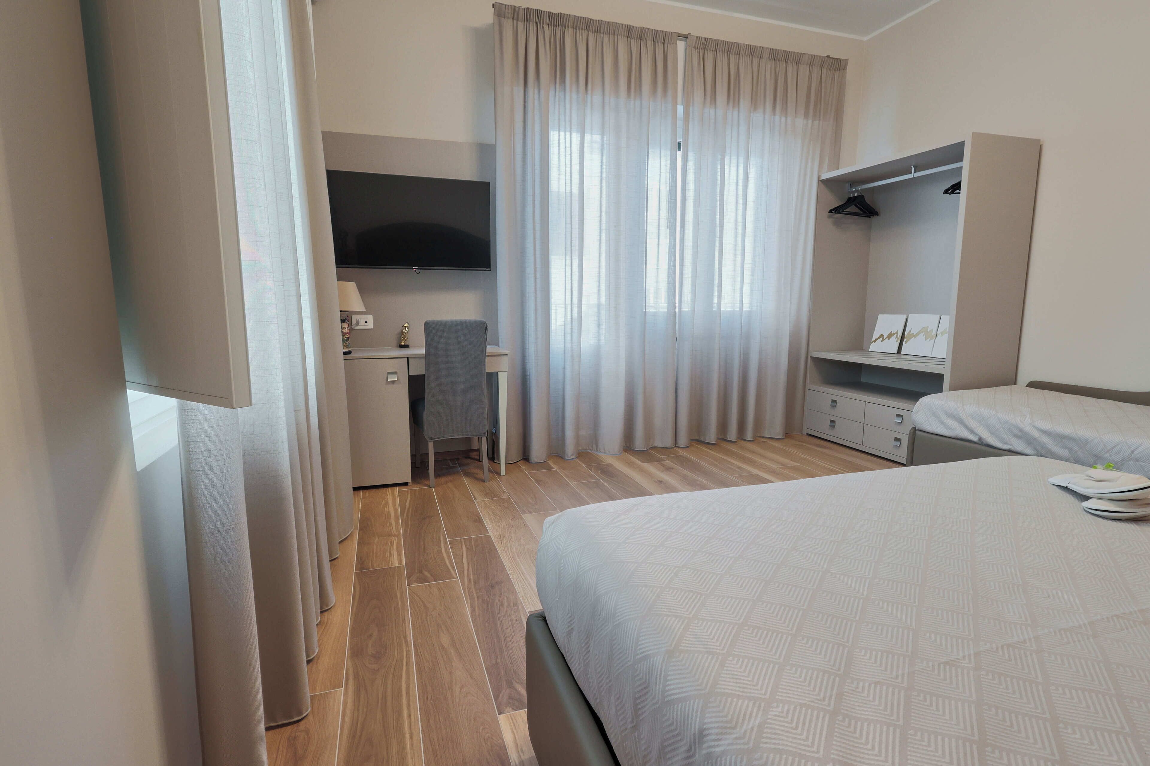A hotel room with a bed, a desk, a chair, a TV, and a wardrobe.