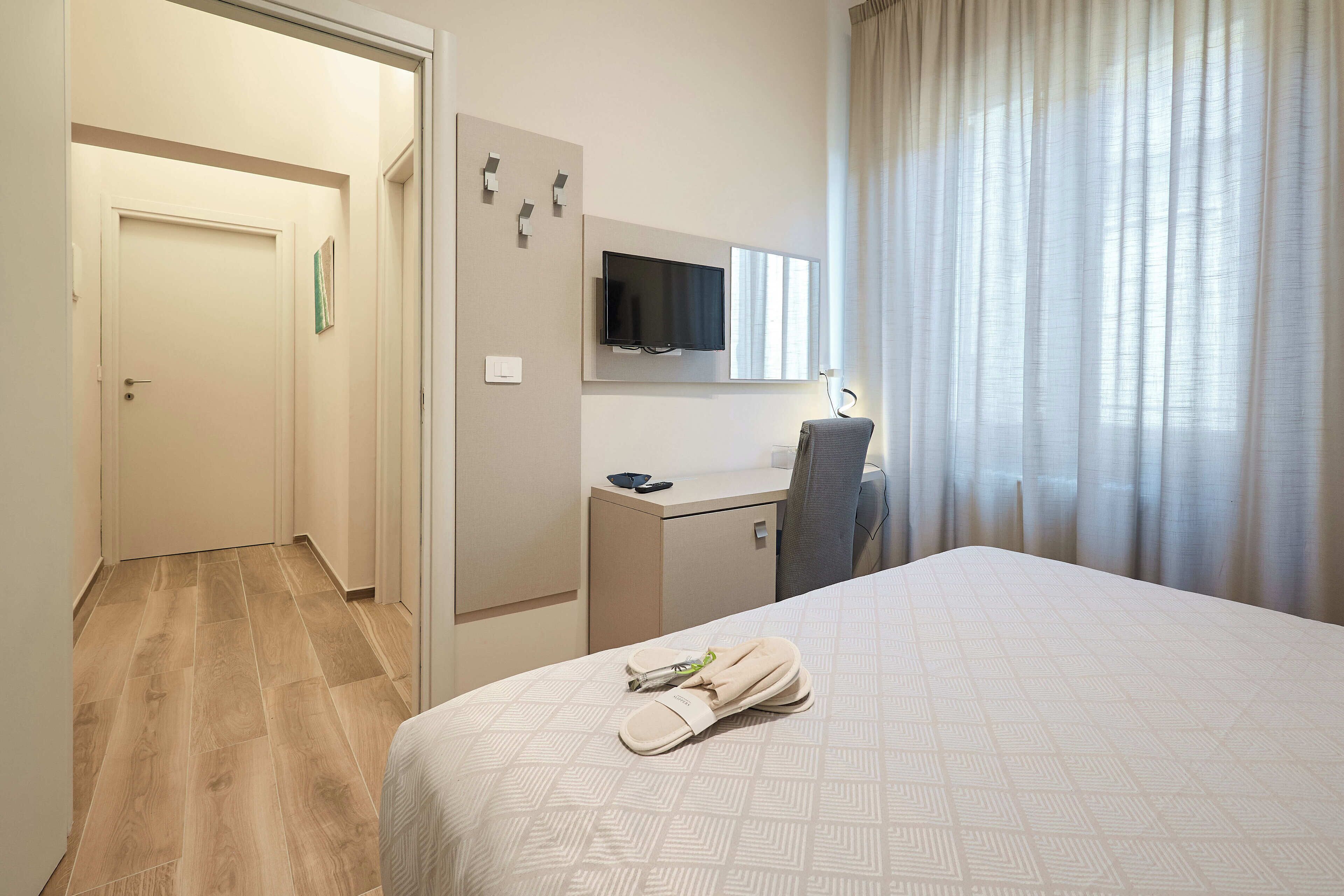 Habitación de hotel con cama, escritorio, televisor y ventana con cortinas.