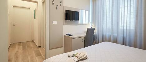 Habitación de hotel con cama, escritorio, televisor y ventana con cortinas.