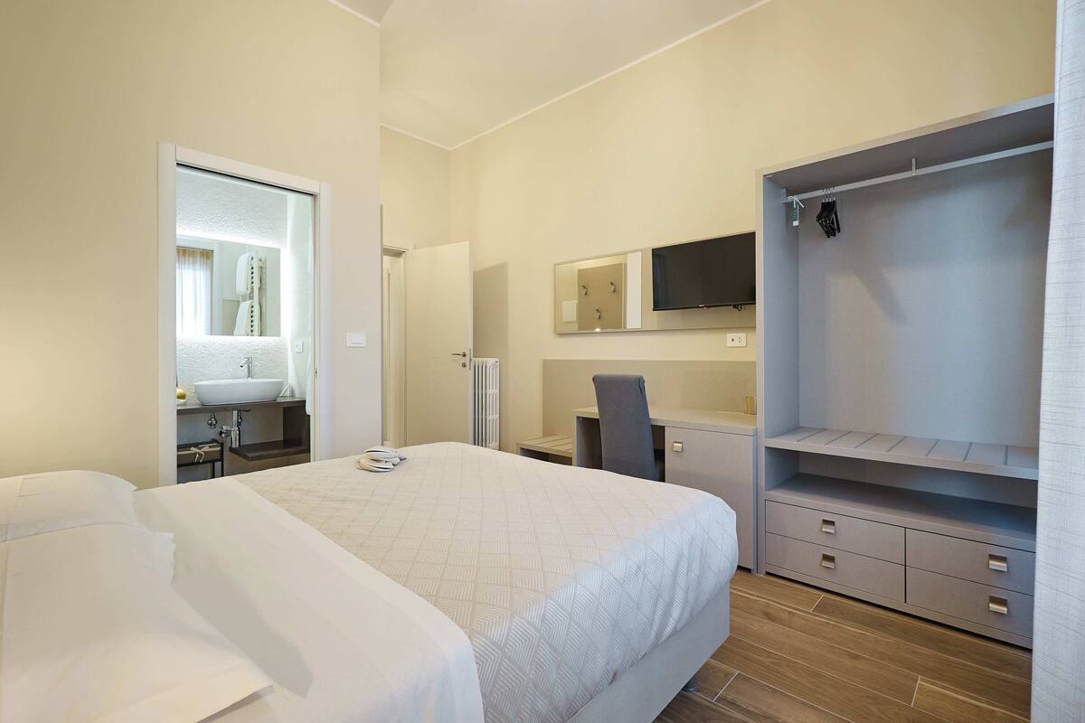 A hotel room with a bed, a desk, a chair, a wardrobe, and a mirror.
