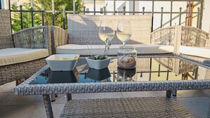 A wicker outdoor seating area with cushions, a glass table, and two wine glasses.