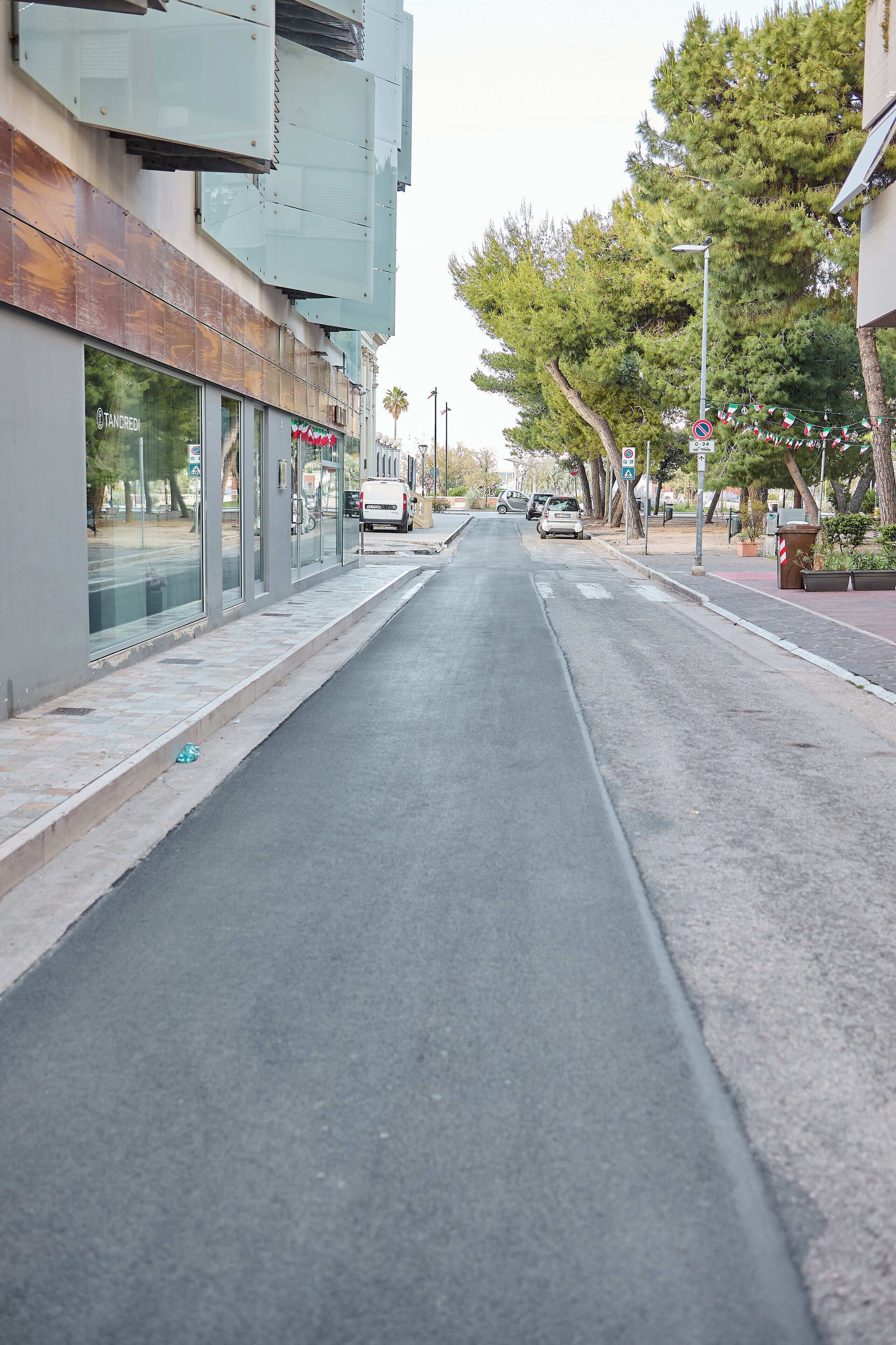 A street with a sidewalk, parked cars, and a building with glass doors.