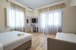 Una camera d'albergo con due letti, una scrivania, una sedia, una televisione e tende.