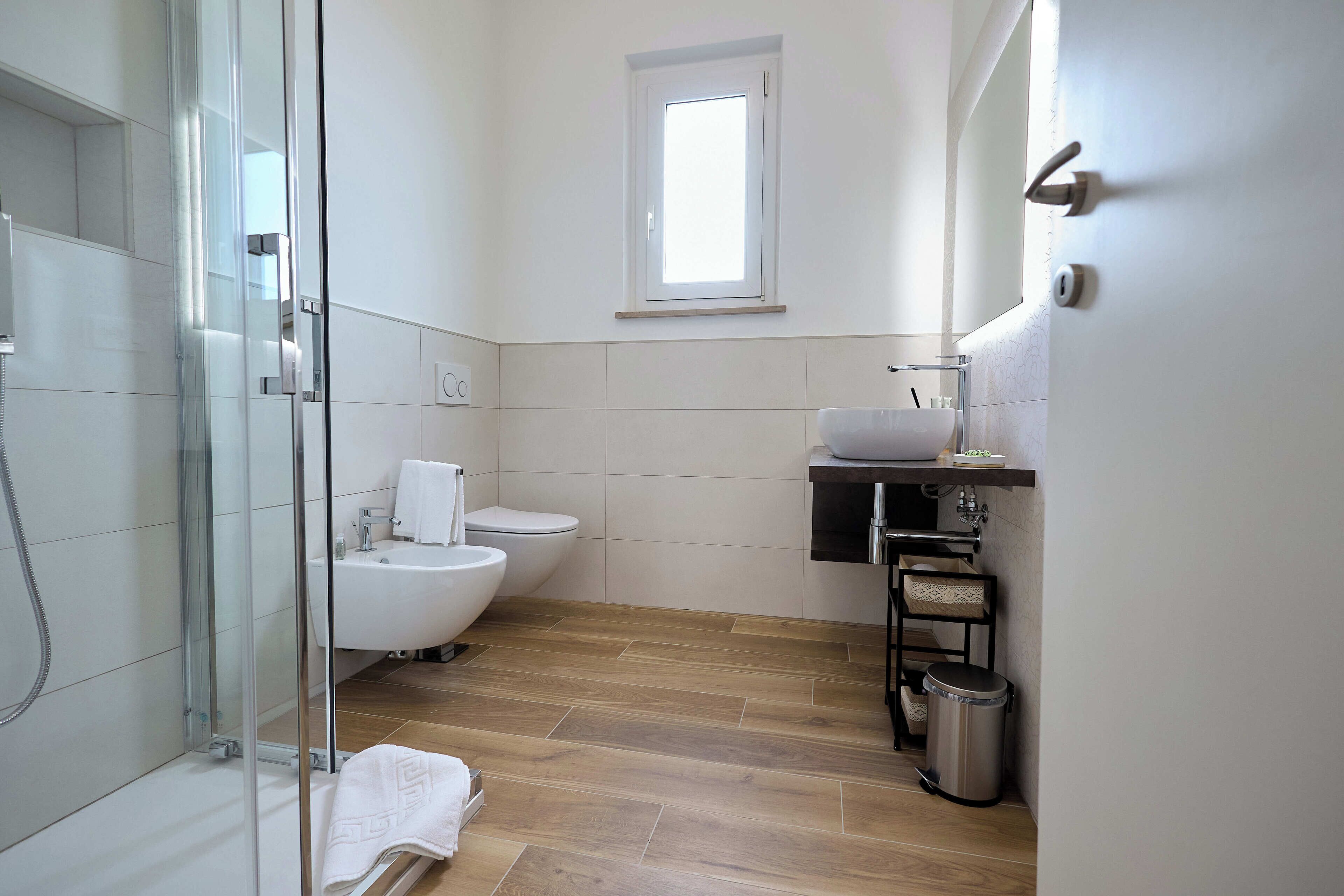 A modern bathroom with a glass shower enclosure, a toilet, a bidet, and a sink with a mirror.