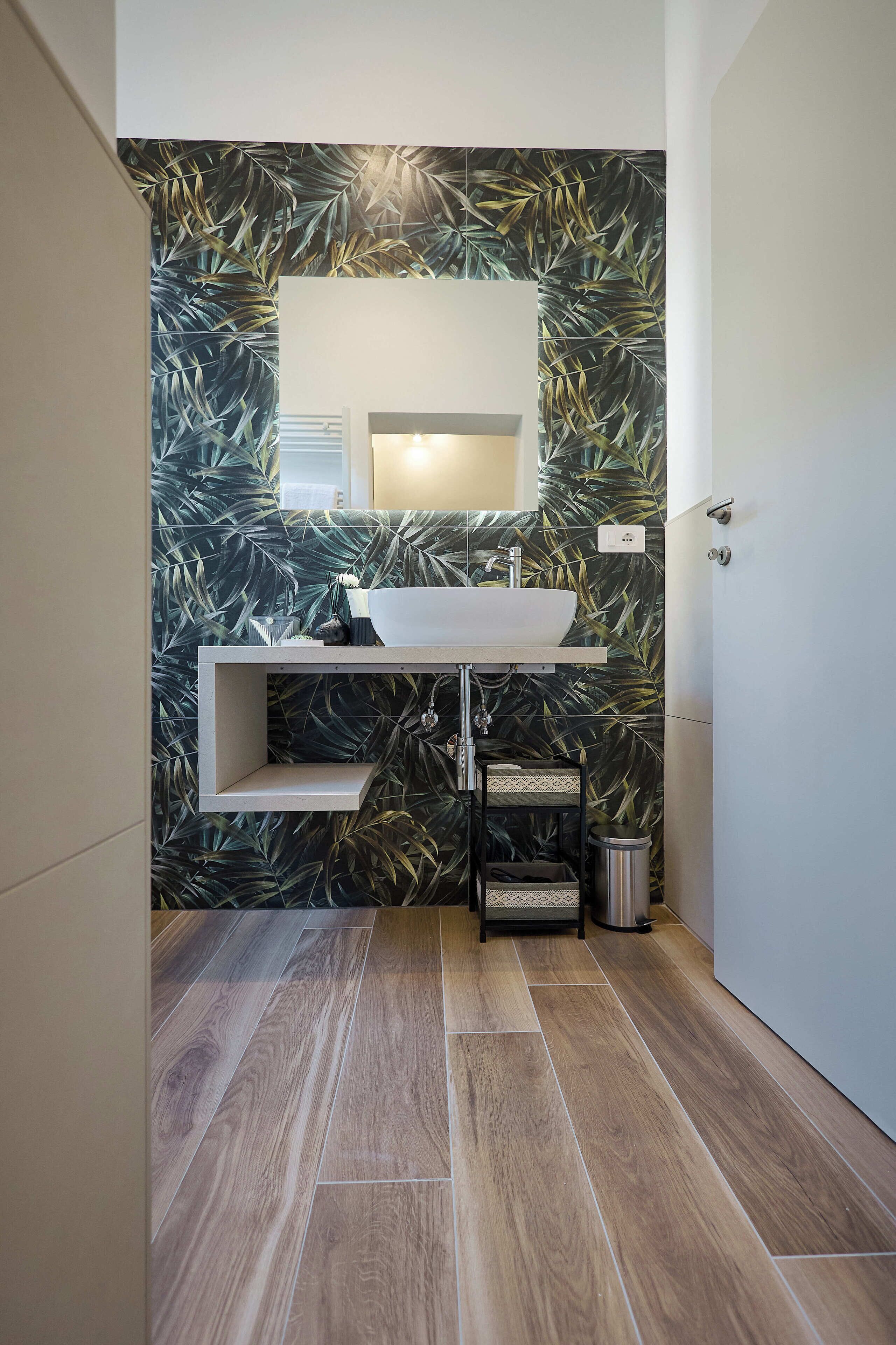 A bathroom with a modern design, featuring a large mirror, a white sink, and a decorative leaf-patterned wall.
