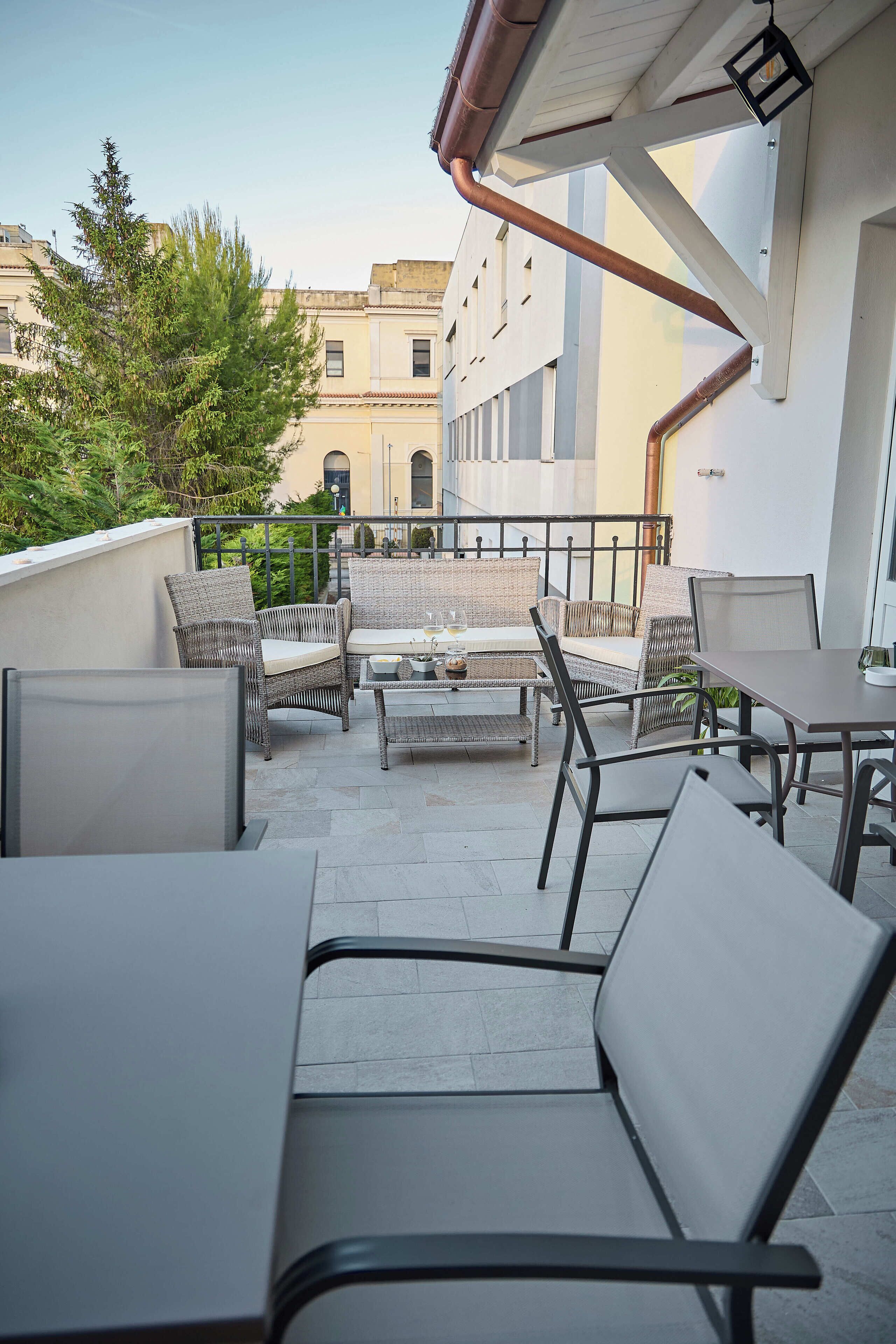 Un patio al aire libre con mobiliario de mimbre, una mesa y vistas a edificios al fondo.