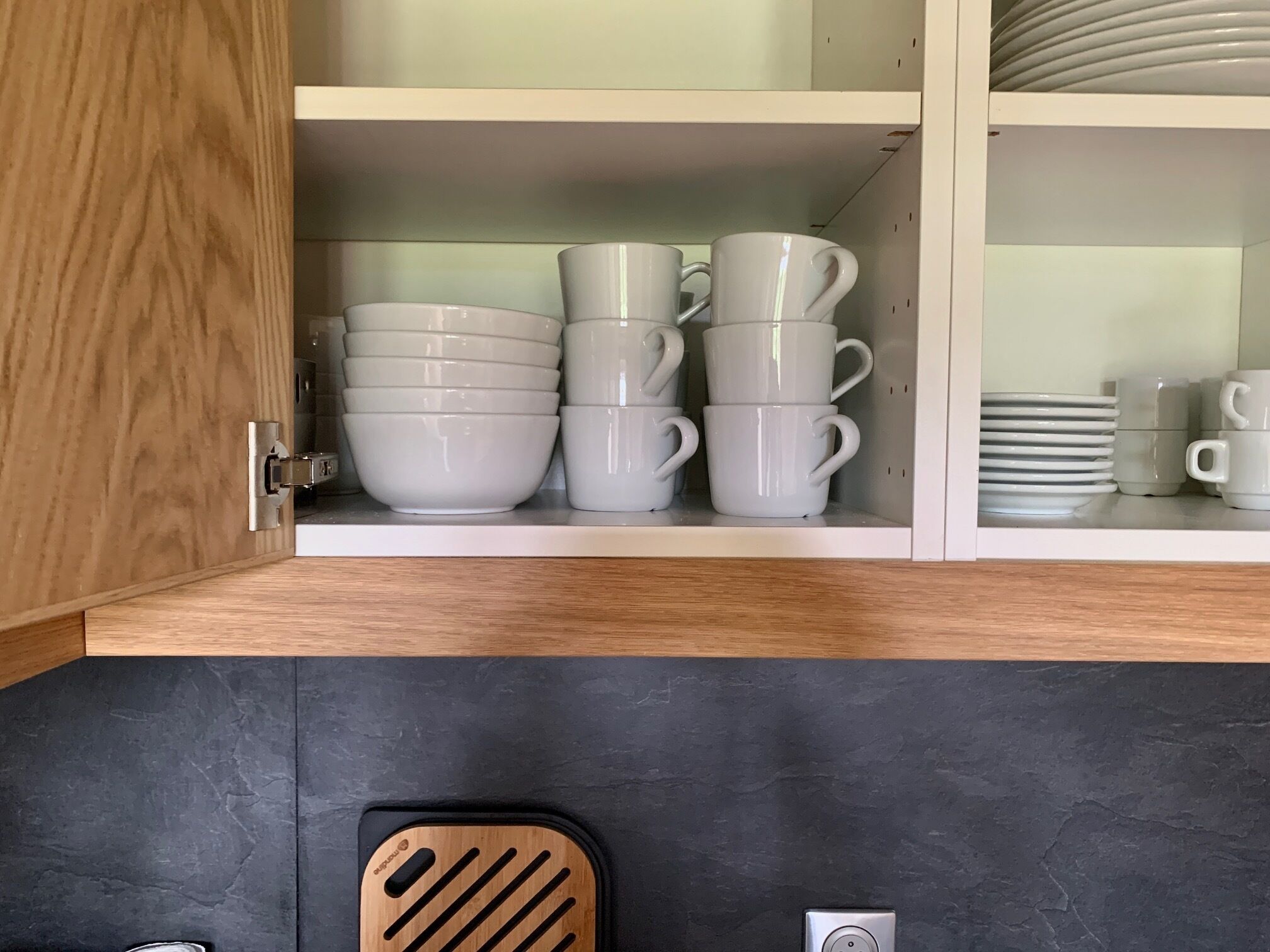 A kitchen cabinet with white ceramic dishes and cups.