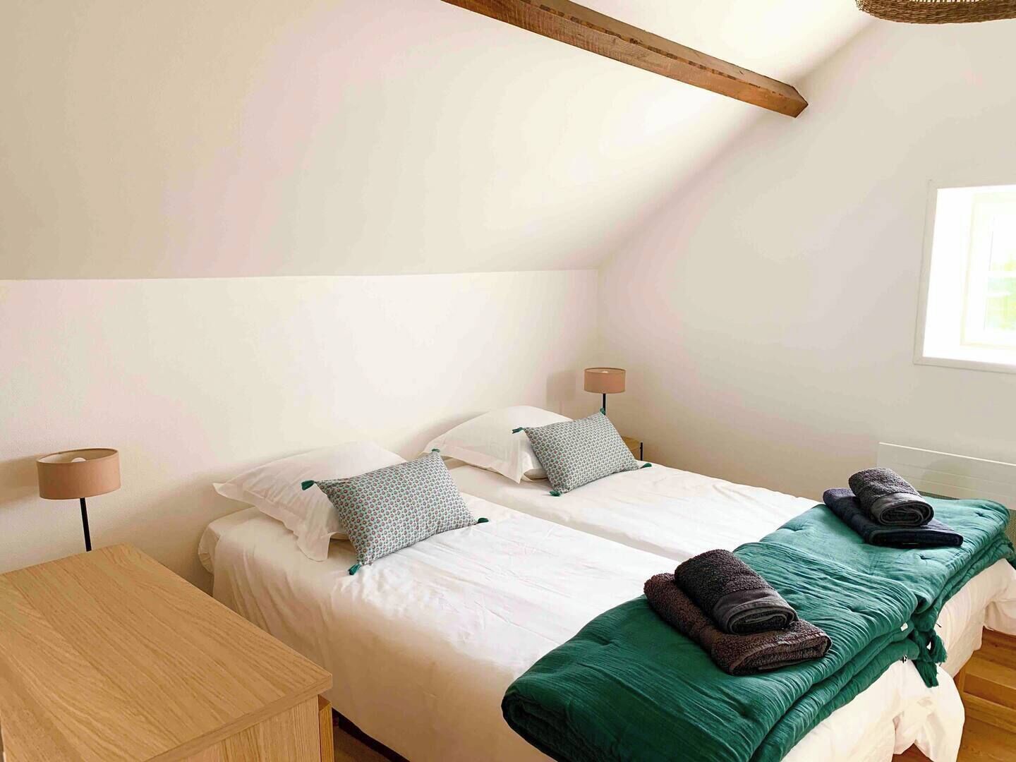 A bedroom with two beds, a wooden table, and a lamp.