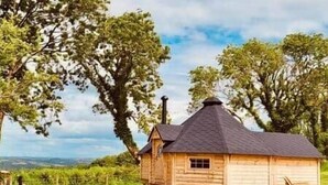 A wooden cabin with a conical roof, surrounded by lush greenery and trees. - Stairway to Devon - Tarka Cabin (Umberleigh)