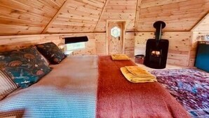 A cozy cabin room with a bed, a fireplace, and a window. - Stairway to Devon - Tarka Cabin (Umberleigh)