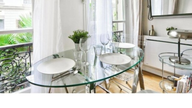Un comedor moderno con una mesa de vidrio, platos blancos y copas transparentes.