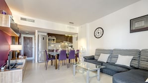 A modern living room with a sofa and a glass coffee table, a dining area with purple chairs, and a kitchen in the background. - MARINES MESTRAL 3 5 Roses (Rosas / Roses)
