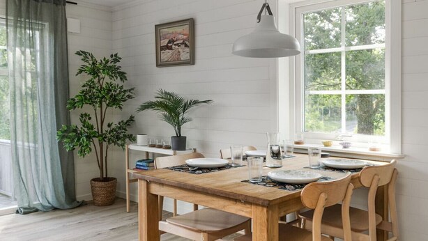 A dining area with a wooden table, chairs, a hanging light, a window with a view, and a potted plant. - Lakeview spacious family home (Västra Götalands län)