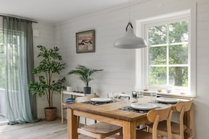 A dining area with a wooden table, chairs, a hanging light, a window with a view, and a potted plant. - Lakeview spacious family home (Västra Götalands län)