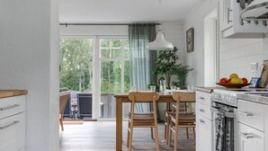 A modern kitchen with wooden cabinets, a dining table with chairs, a large window with a view of trees, and a hanging light fixture. - Lakeview spacious family home (Västra Götalands län)