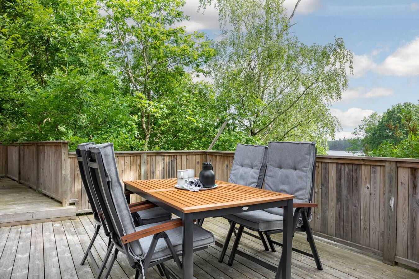 An outdoor patio with a wooden table and two chairs, surrounded by a wooden fence and lush greenery.