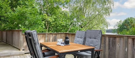 An outdoor patio with a wooden table and two chairs, surrounded by a wooden fence and lush greenery.