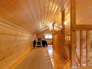 Ein Holzinnenraum mit schrägverdeckter Decke, einem Bett mit dunkler Bettdecke, einem Sessel und einem Fenster.