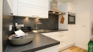 Una cocina moderna con armarios blancos, encimera negra, pileta de acero inoxidable y horno integrado.