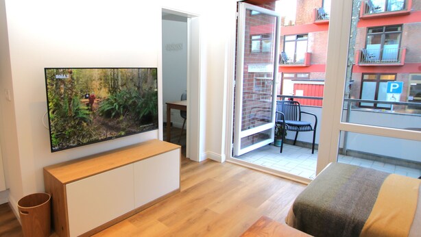 Una sala de estar moderna con un televisor de pantalla plana grande montado en la pared, un banco de madera y una pequeña mesa con posavasos de madera.