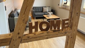 Une structure en bois avec le mot « HOME » en évidence au premier plan, un canapé gris et une table basse à l’arrière-plan.