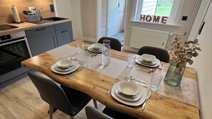 Une cuisine moderne avec une table à manger en bois, dressée pour quatre personnes, et agrémentée de la vaisselle de base et d’un vase contenant des fleurs séchées.