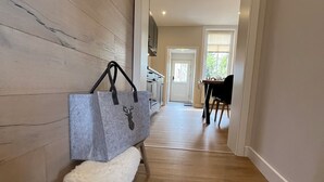 Un couloir avec un plancher en bois, un banc sur lequel se trouve un sac gris, et un coin repas avec une table et des chaises.