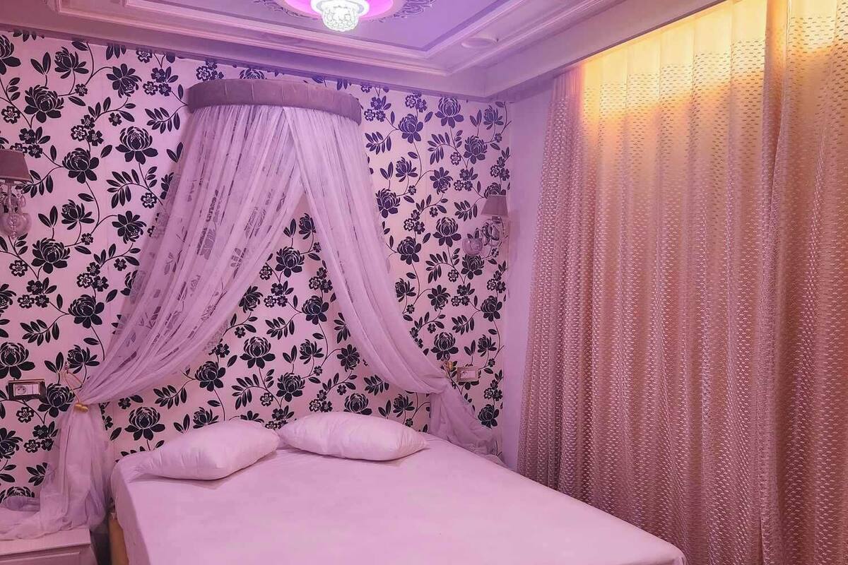 Un dormitorio con cama a dosel, papel tapiz floral e iluminación decorativa en el techo.