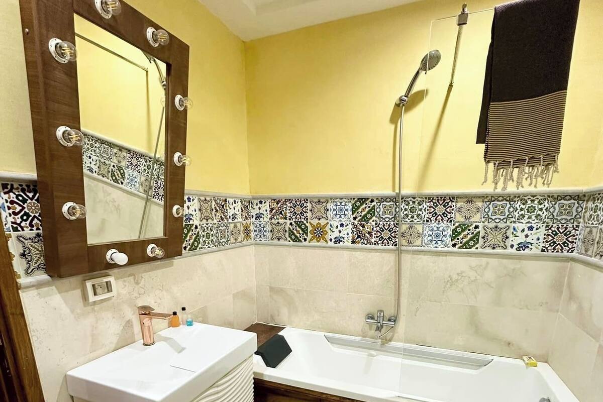 Un baño con lavamanos blanco, un espejo grande iluminado, bañera y ducha.