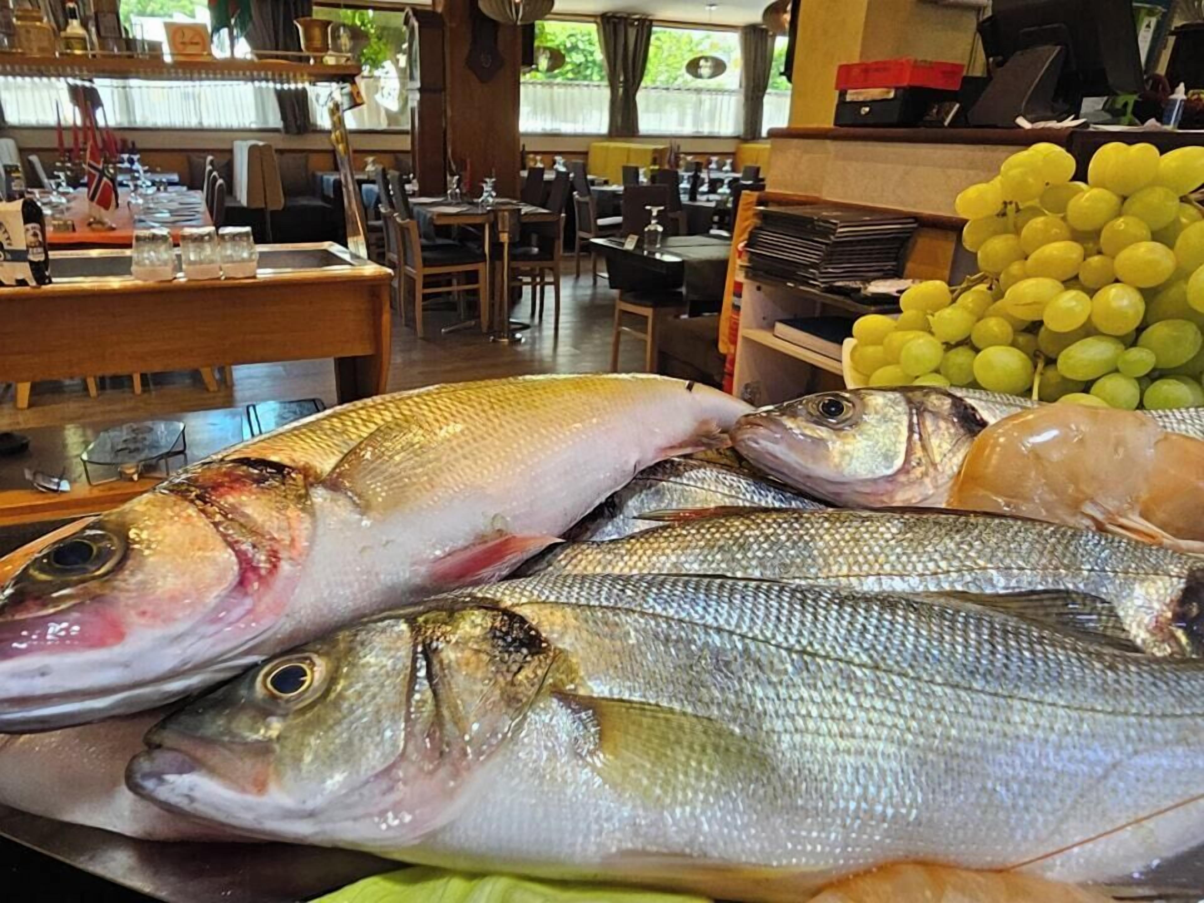 A seafood display with various fish and a bunch of yellow grapes in a restaurant setting.