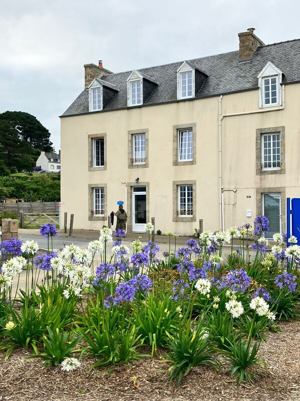 A two-story building with a beige facade, multiple windows, and a stone chimney. - A Bord de mer ! Grande Maison Face à la mer (Plougasnou)