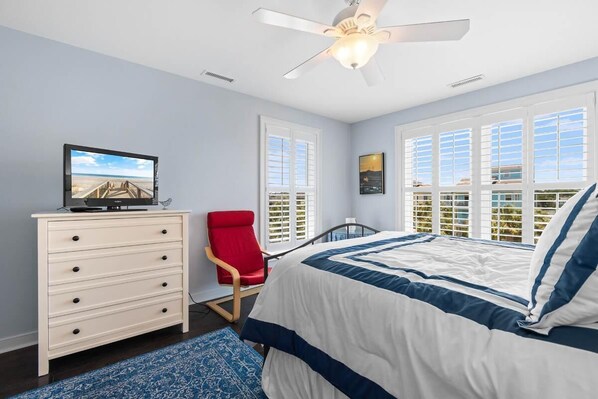 Une chambre à coucher avec un lit, une commode, un fauteuil rouge et un ventilateur de plafond.