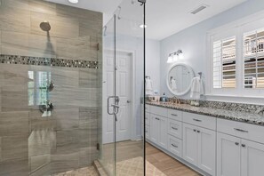 A modern bathroom with a glass shower enclosure, white cabinetry, and a large mirror above the sink.