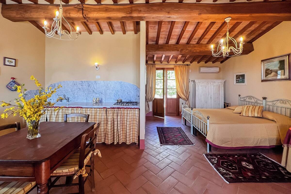 Ein Zimmer mit Holzboden, einem Esstisch mit Stühlen, einer Küchenzeile mit Herd und einem Bett mit Kopfteil.