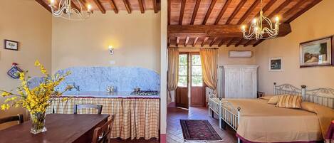 A room with a wooden ceiling, a dining table with chairs, a kitchen area with a stove, and a bed with a headboard.