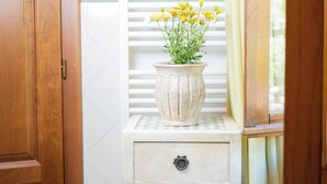 A wooden door, a white tiled wall, a white radiator, a white tiled table with a white vase of yellow flowers, and a white drawer with a metal handle. - Agriturismo Cima alla Serra (Buti)