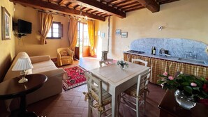 A cozy room with a wooden ceiling, a dining table, a sofa, a TV, and a kitchen area with a marble backsplash. - Agriturismo Cima alla Serra (Buti)