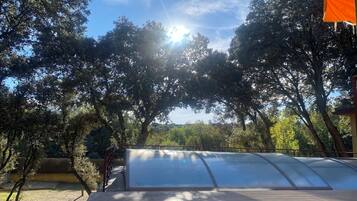 Un espacio al aire libre techado con techo transparente, rodeado de árboles y cielo despejado.
