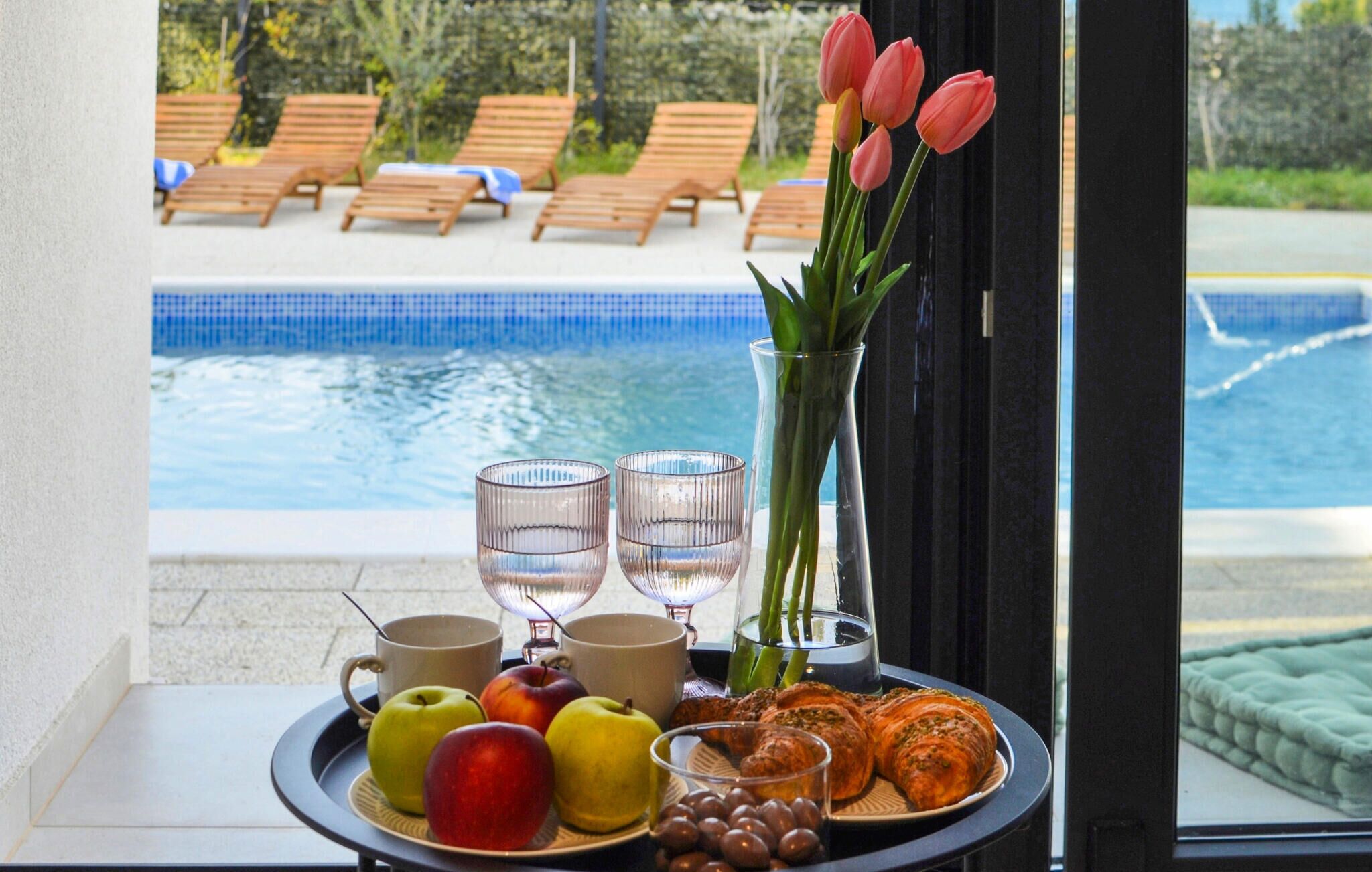 Ein Tisch mit Früchten, Croissants und einem Strauß Tulpen am Poolrand.